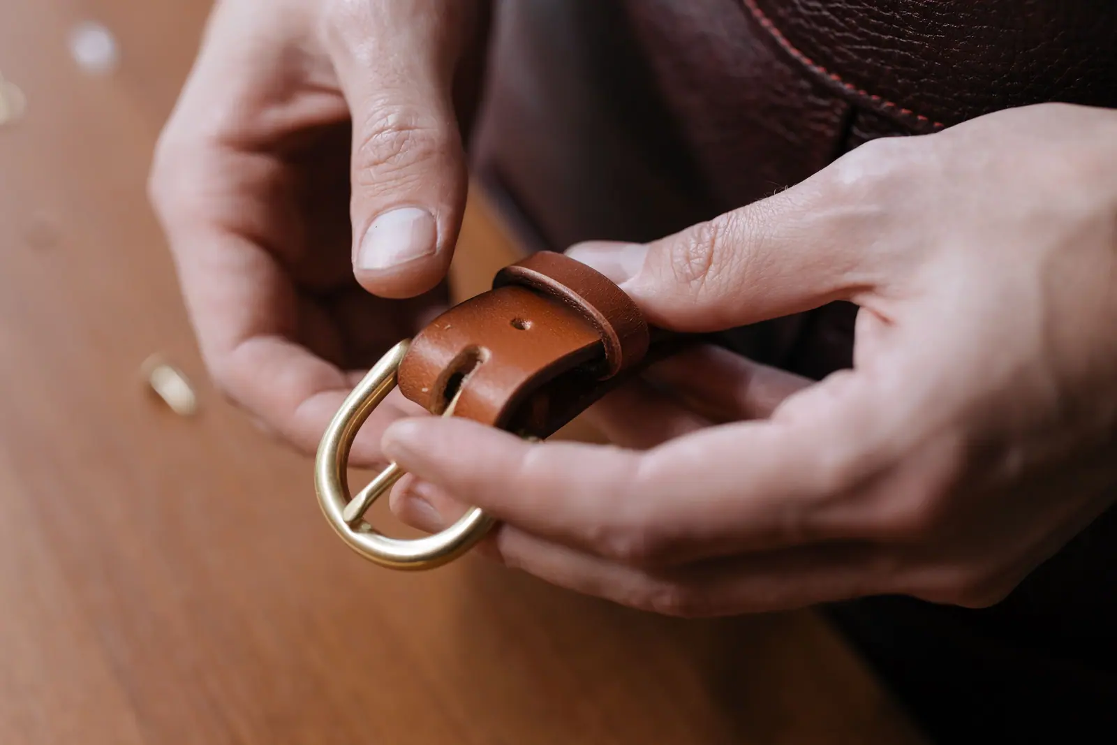 Hands fastening a brass buckle on a tan leather belt.