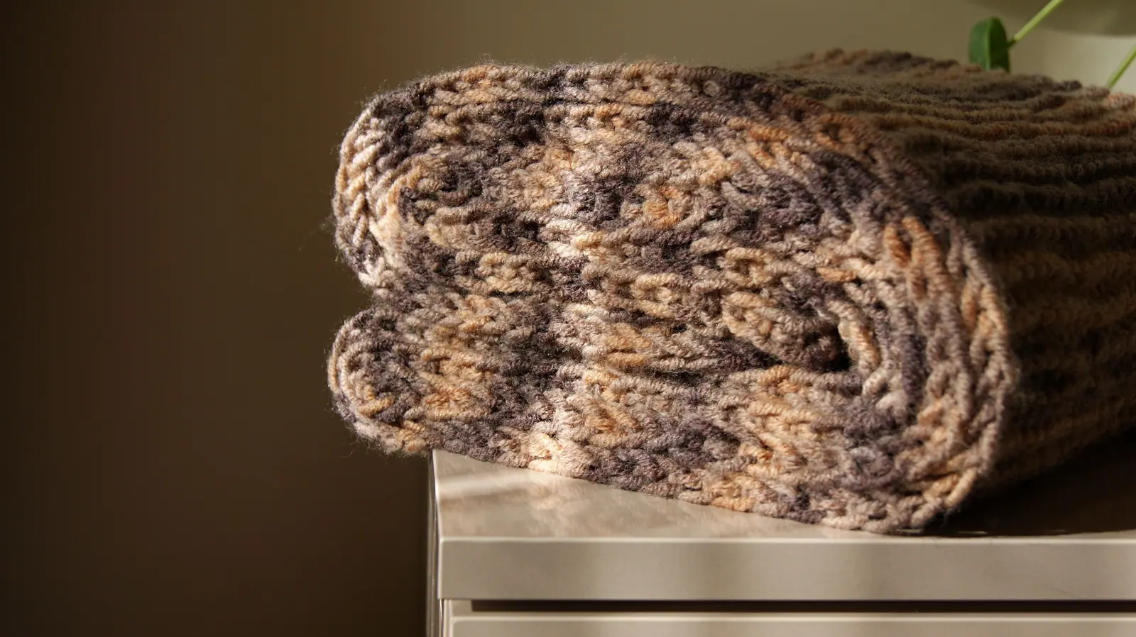 A folded hand-crocheted scarf in brown and cream on a small table.