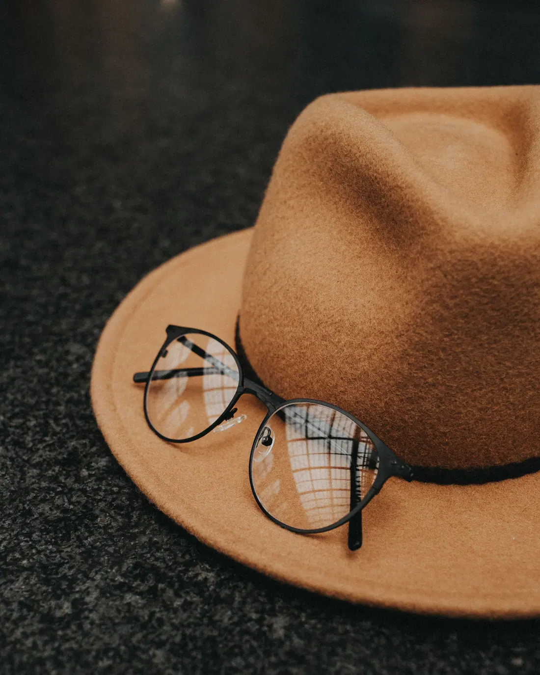 A camel felt hat with a pair of round spectacles resting on the brim.