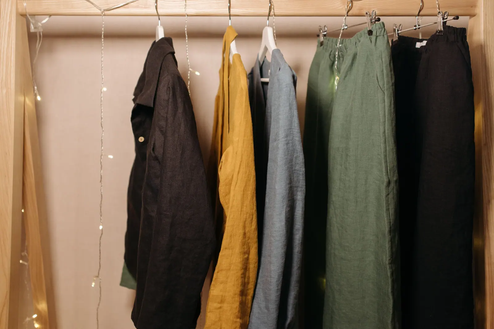 Linen shirts and trousers in black, mustard, grey and olive on a timber rail.